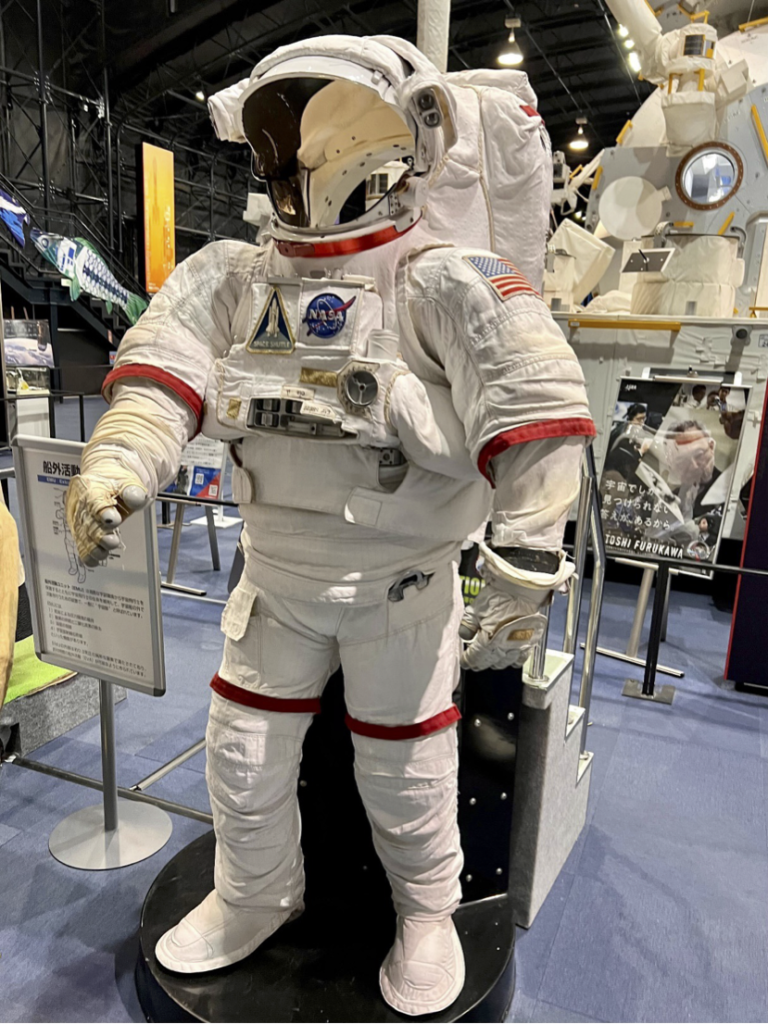 白い宇宙服の模型。首周り、袖周り、太ももの周りに赤いラインが入っており、左肩にはアメリカの国旗、胸の部分にはNASAのパッチが付いています