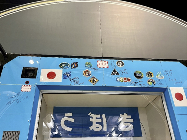 水色のゲートの上部に日本の国旗や宇宙ミッションのパッチが無数に貼ってあり、宇宙飛行士のサインも書かれています