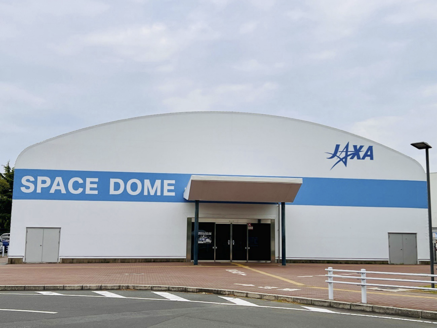 かまぼこ型の建物があり、壁面にJAXAのロゴ、「SPACE DOME」の文字が記載されています